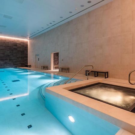 Citysuites 2 Aparthotel 맨체스터 외부 사진 The photo shows an indoor swimming pool area. The pool is a bright blue color and features smooth, tiled surfaces. On one side, there is a hot tub area with steps leading into it. The walls are made of light-colored stone, and there is ambient lighti
