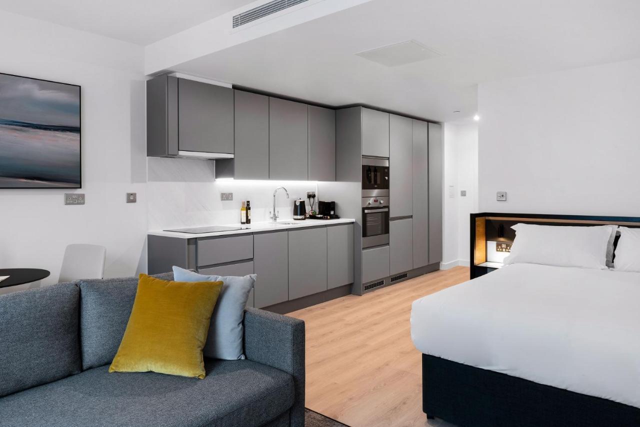Citysuites 2 Aparthotel 맨체스터 외부 사진 The photo shows a modern studio apartment featuring an open-plan layout. On one side, there is a kitchenette with sleek, gray cabinets and appliances, including a coffee maker and oven. Adjacent to the kitchenette is a small dining area with a table 