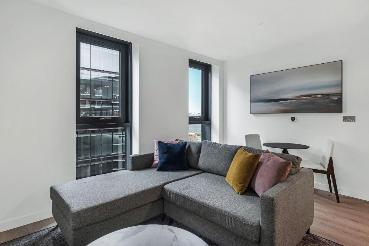 Citysuites 2 Aparthotel 맨체스터 외부 사진 The photo shows a modern living space featuring a gray sectional sofa adorned with colorful throw pillows. There are large windows allowing natural light to fill the room, offering a view of the outdoors. A wall-mounted television is positioned above