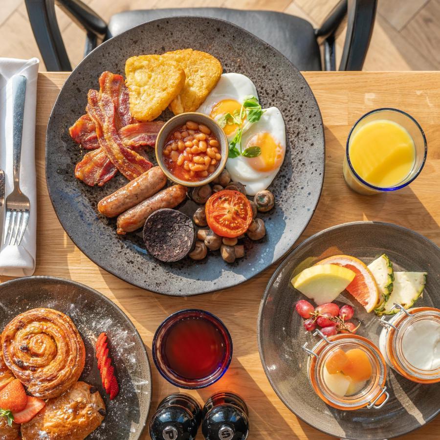 Citysuites 2 Aparthotel 맨체스터 외부 사진 The photo showcases a delicious breakfast spread. On a large, dark plate, there are items including crispy bacon, two fried eggs, baked beans, a grilled tomato, sautéed mushrooms, sausage links, and slices of black pudding. There's also a few pieces 