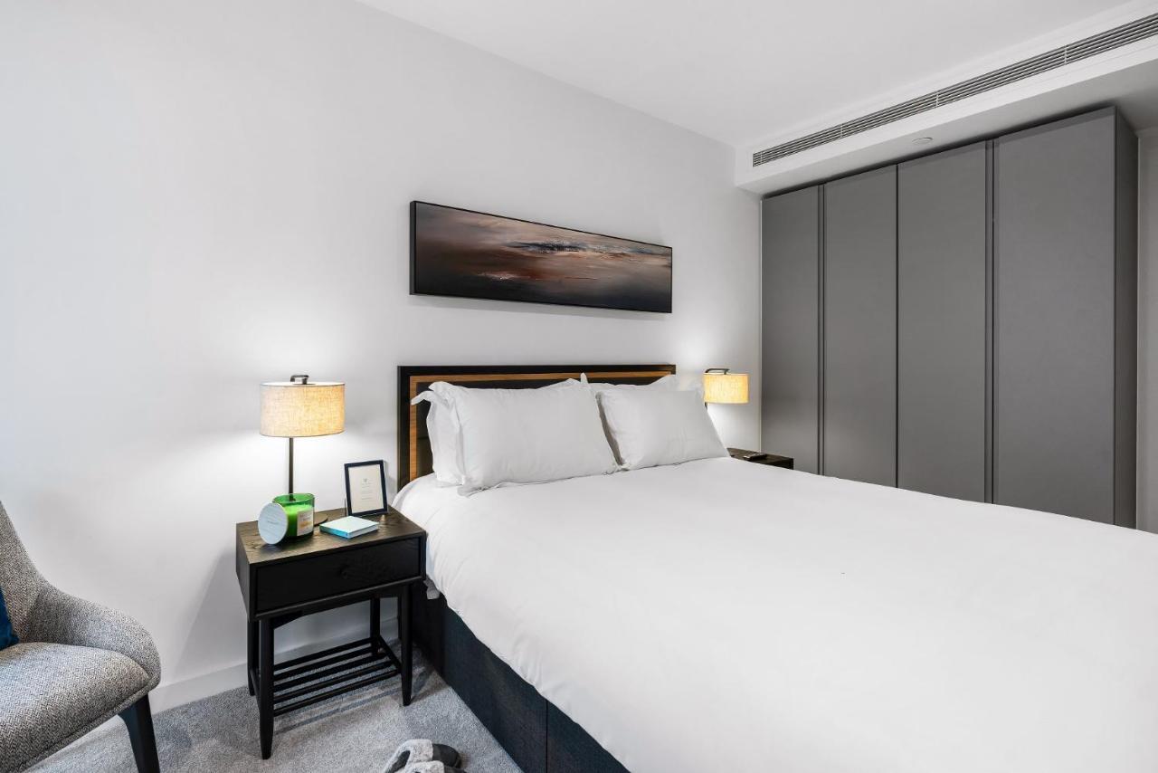 Citysuites 2 Aparthotel 맨체스터 외부 사진 The photo shows a modern bedroom with a neatly made bed featuring white linens and pillows. Flanking the bed are two bedside tables, each with a lamp providing soft lighting. There is a piece of artwork above the bed, which appears to depict a landsc