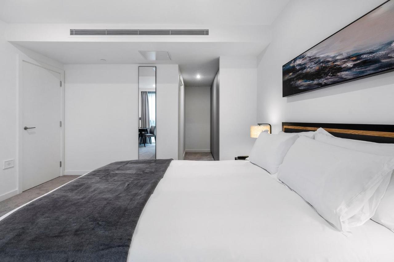 Citysuites 2 Aparthotel 맨체스터 외부 사진 The photo shows a modern bedroom with a minimalistic design. In the foreground, there is a neatly made bed with white linens and a dark gray throw blanket. To the side, there is a bedside lamp and a piece of abstract artwork on the wall above the bed