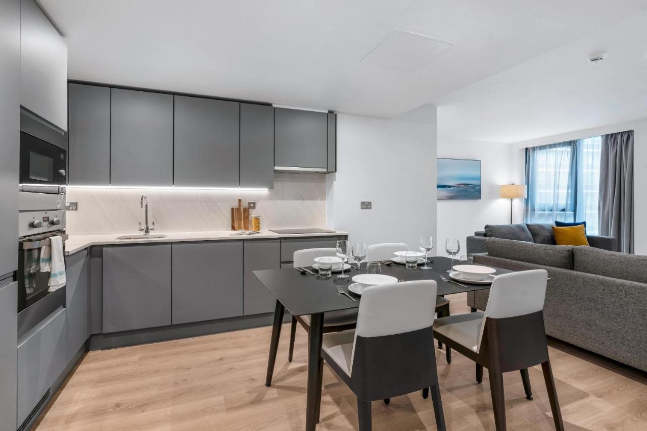 Citysuites 2 Aparthotel 맨체스터 외부 사진 The photo shows a modern, open-concept kitchen and living area. The kitchen features sleek, gray cabinetry with a countertop, a sink, and built-in appliances. There are cooking utensils displayed on the countertop. Next to the kitchen, there is a din