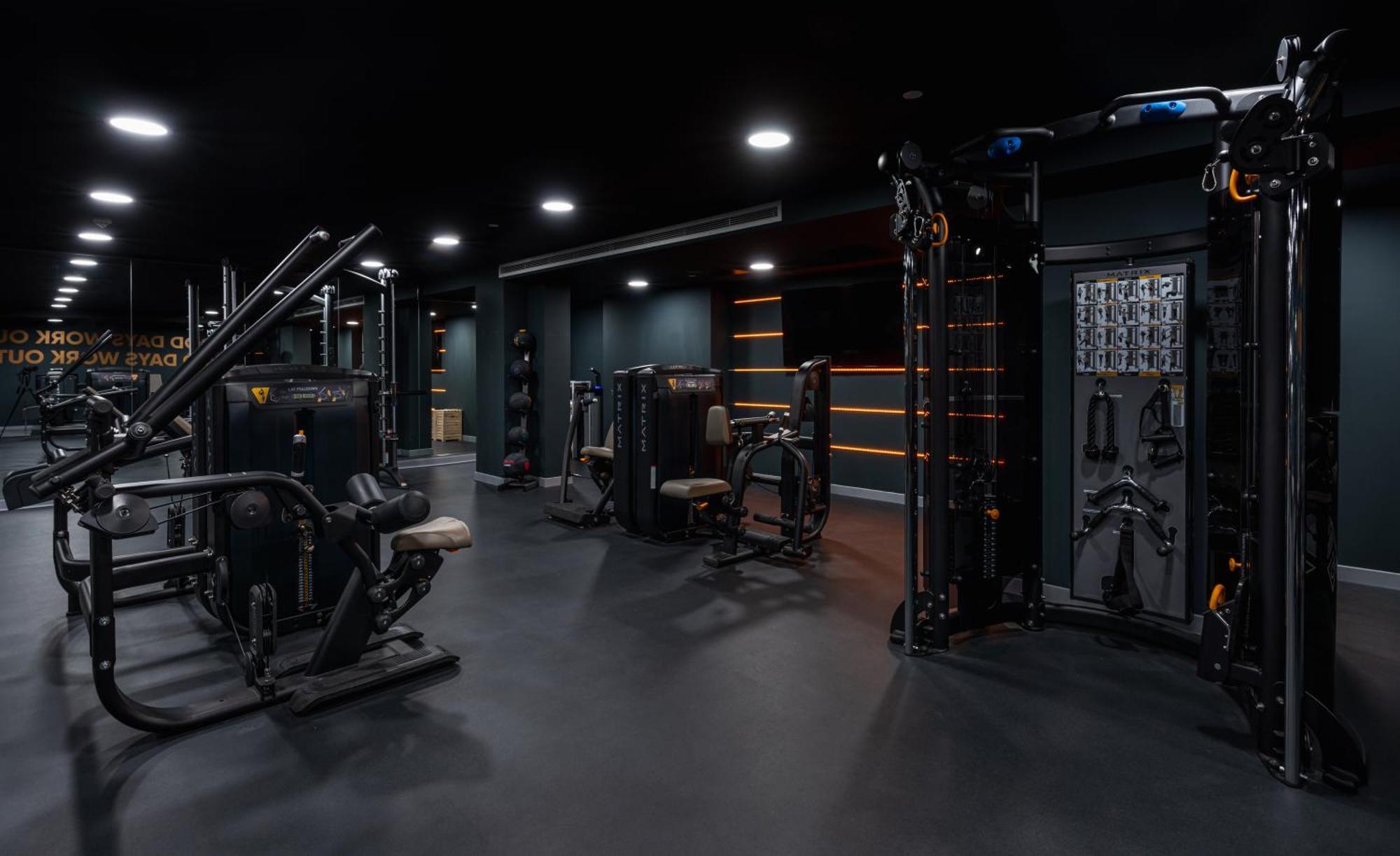 Citysuites 2 Aparthotel 맨체스터 외부 사진 The photo shows a modern gym or fitness area with various workout machines. The space has a dark color scheme, featuring black walls and flooring. There are multiple pieces of exercise equipment, including stations for strength training, possibly tar
