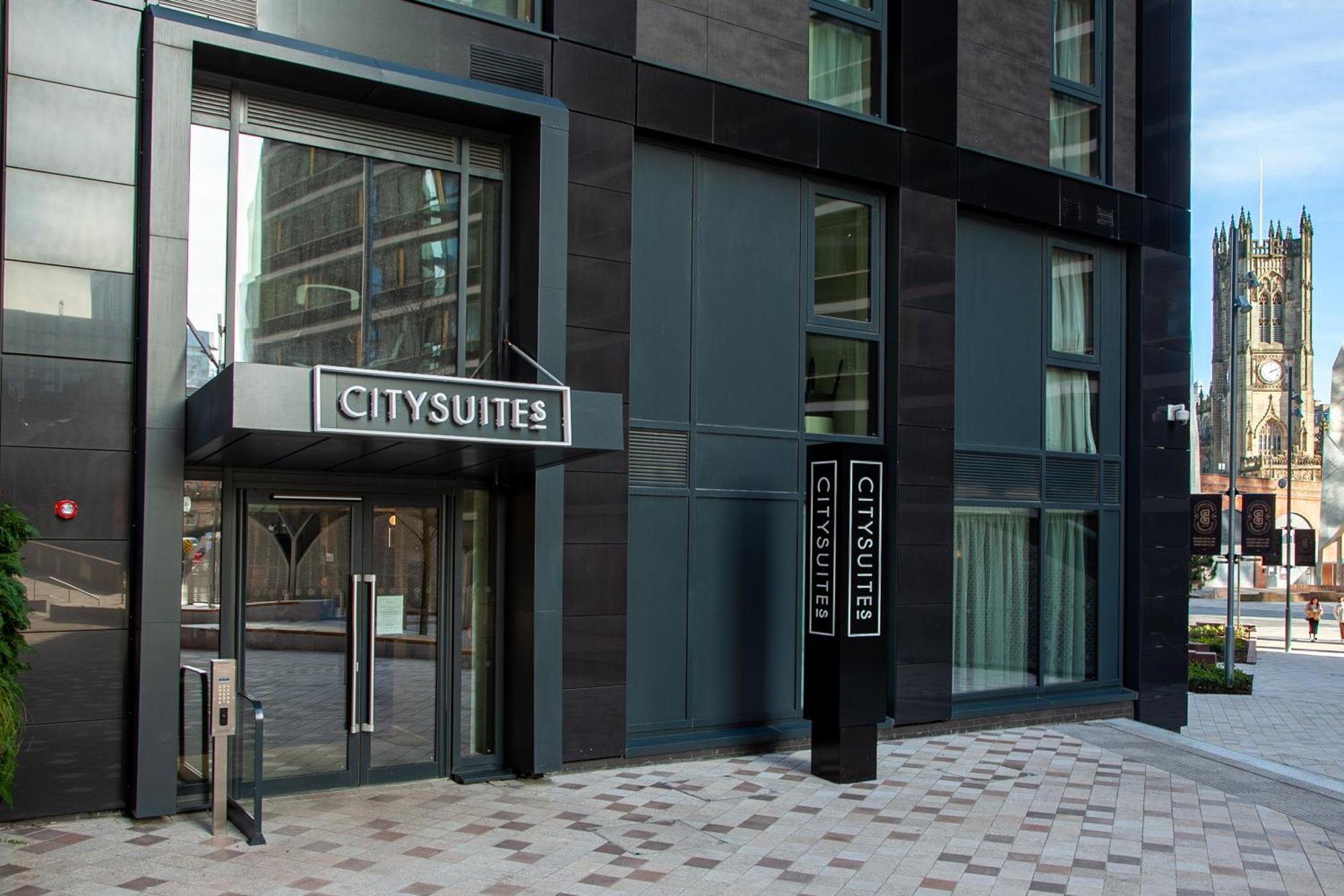 Citysuites 2 Aparthotel 맨체스터 외부 사진 The photo shows the entrance to a modern building labeled "CITYSUITES." The entrance features large glass doors and a sleek, contemporary design. The building has dark exterior panels and large windows, suggesting a stylish and urban environment. The