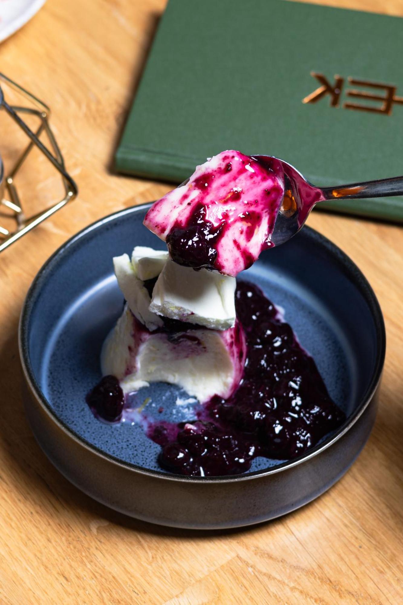 Citysuites 2 Aparthotel 맨체스터 외부 사진 The photo shows a serving of dessert, likely a type of panna cotta or a creamy custard, partially dished out and accompanied by a rich berry sauce, possibly made from blueberries or blackberries. A spoon with some of the dessert and sauce is hovering